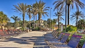 Un espace aménagé au bord de la piscine, avec des chaises longues et des palmiers.