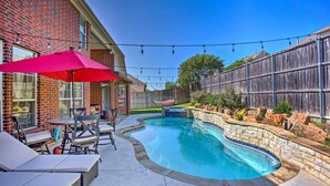 A backyard with a swimming pool, patio furniture, and a red umbrella. - Private Pool & Hot Tub: Spacious Murphy Getaway (Plano)
