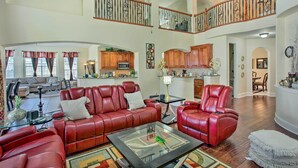 A spacious living area with a red leather sofa, a glass coffee table, and a dining area with wooden cabinets. - Private Pool & Hot Tub: Spacious Murphy Getaway (Plano)