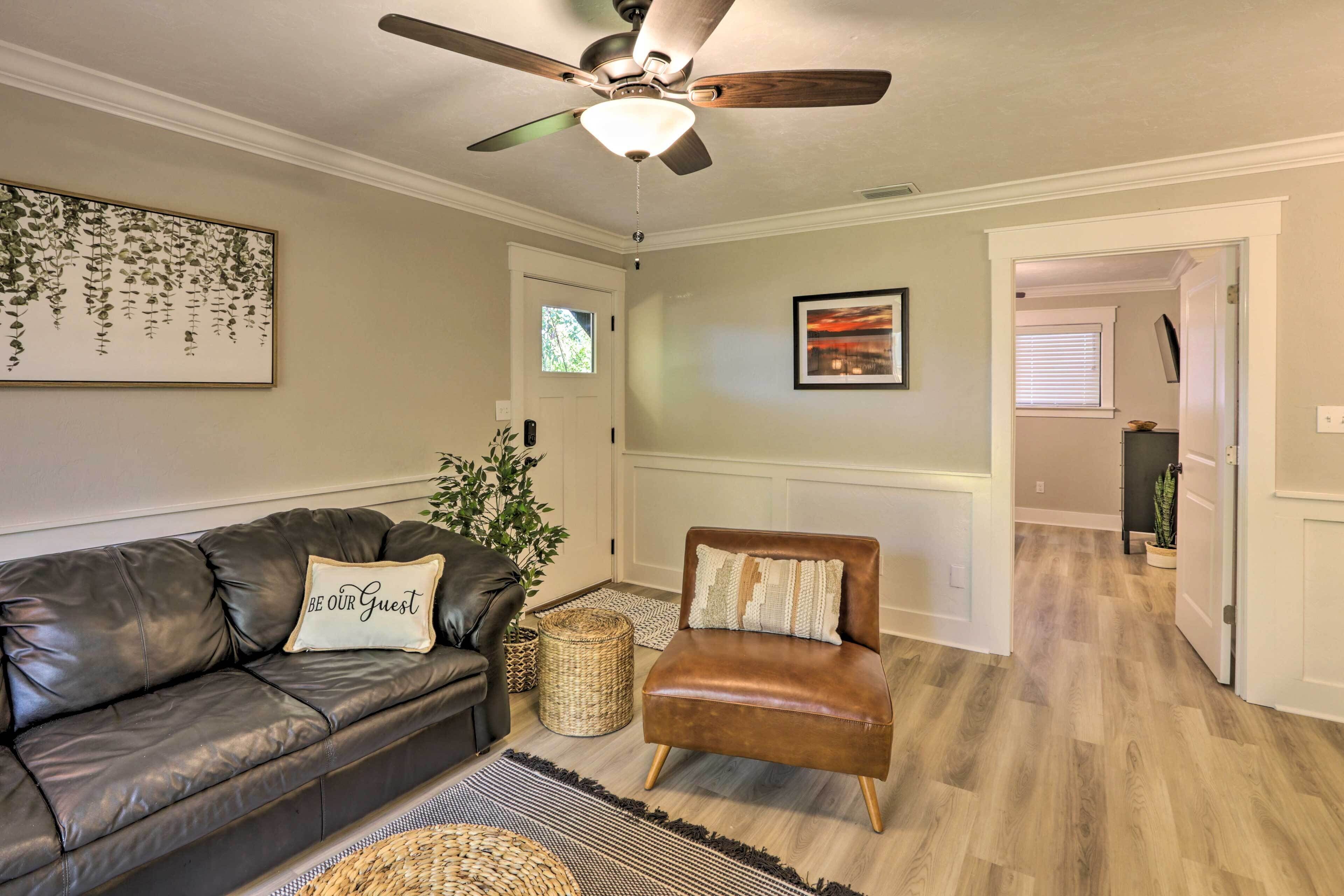 Un salon avec un canapé en cuir, un fauteuil marron, un ventilateur de plafond et un tableau encadré accroché au mur.