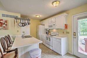 A compact kitchen with white cabinets, a built-in microwave, a stove, and a hanging pot rack.