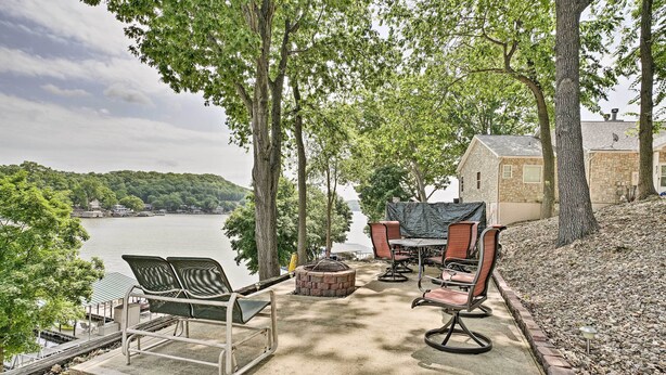 Un espace extérieur aménagé avec des chaises et une table, un foyer et une vue sur un lac et des collines.
