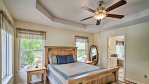 Une chambre à coucher avec un lit en bois, une table de chevet avec une lampe, un ventilateur de plafond et une fenêtre ornée de rideaux en dentelle.