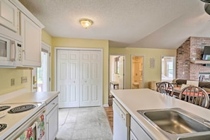 A kitchen with white cabinets, a stove, a sink, and a brick wall. - Private Boat Slip, Dock: Waterfront Lake Ozark Gem (Sunrise Beach)
