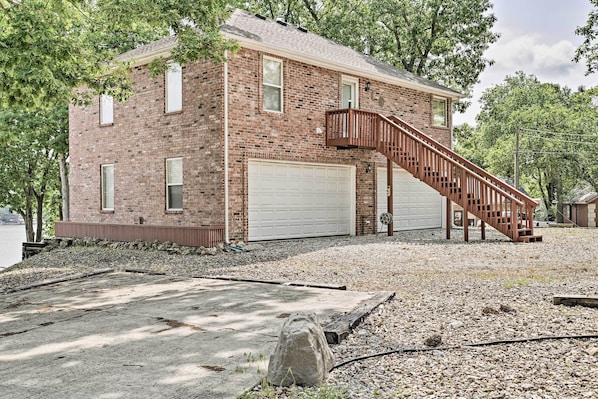 A two-story brick house with a white garage door, a wooden staircase leading to the second floor, and a gravel driveway.