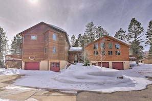 Une maison en bois à deux étages, avec une porte de garage rouge, entourée de neige et d’arbres.