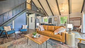 Ein geräumiger Wohnbereich mit einer großen Couch, einem Couchtisch und blauen Sessel. Eine Treppe führt in eine obere Ebene.