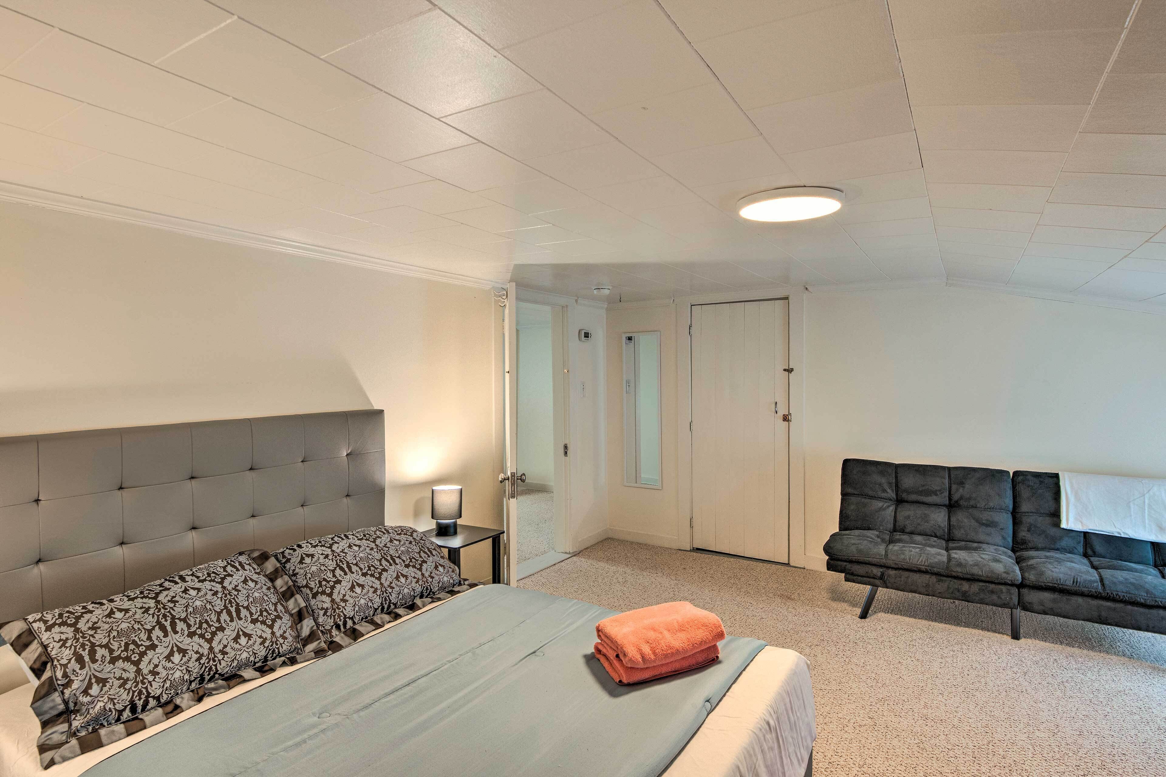A bedroom with a large bed, a sofa, a nightstand, and a door leading to another room.
