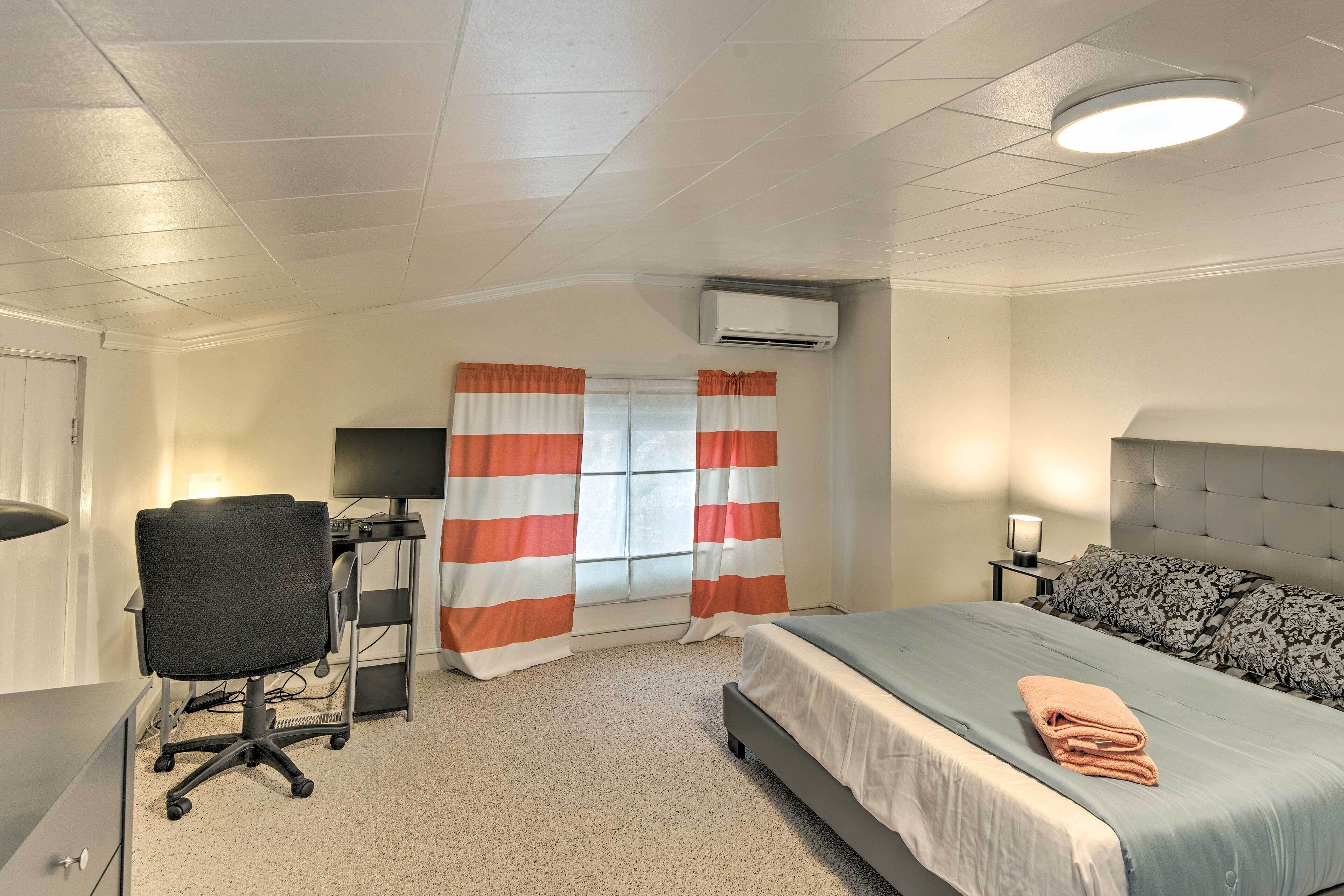 Une chambre à coucher comprenant un lit, un bureau, un climatiseur et une fenêtre avec des rideaux.