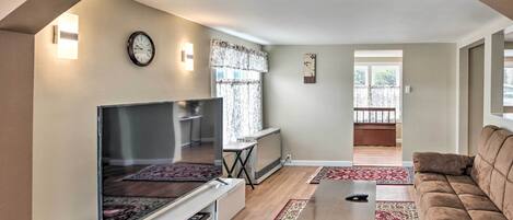 Ein Wohnzimmer mit Flachbildfernseher, einer Couch, einem Couchtisch und einem roten Teppich mit Muster.