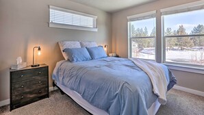 A bedroom with a bed, nightstands, a lamp, and a window with a view of trees. - Modern Bend Home ~ 3 Mi to Old Mill District! (Bend)