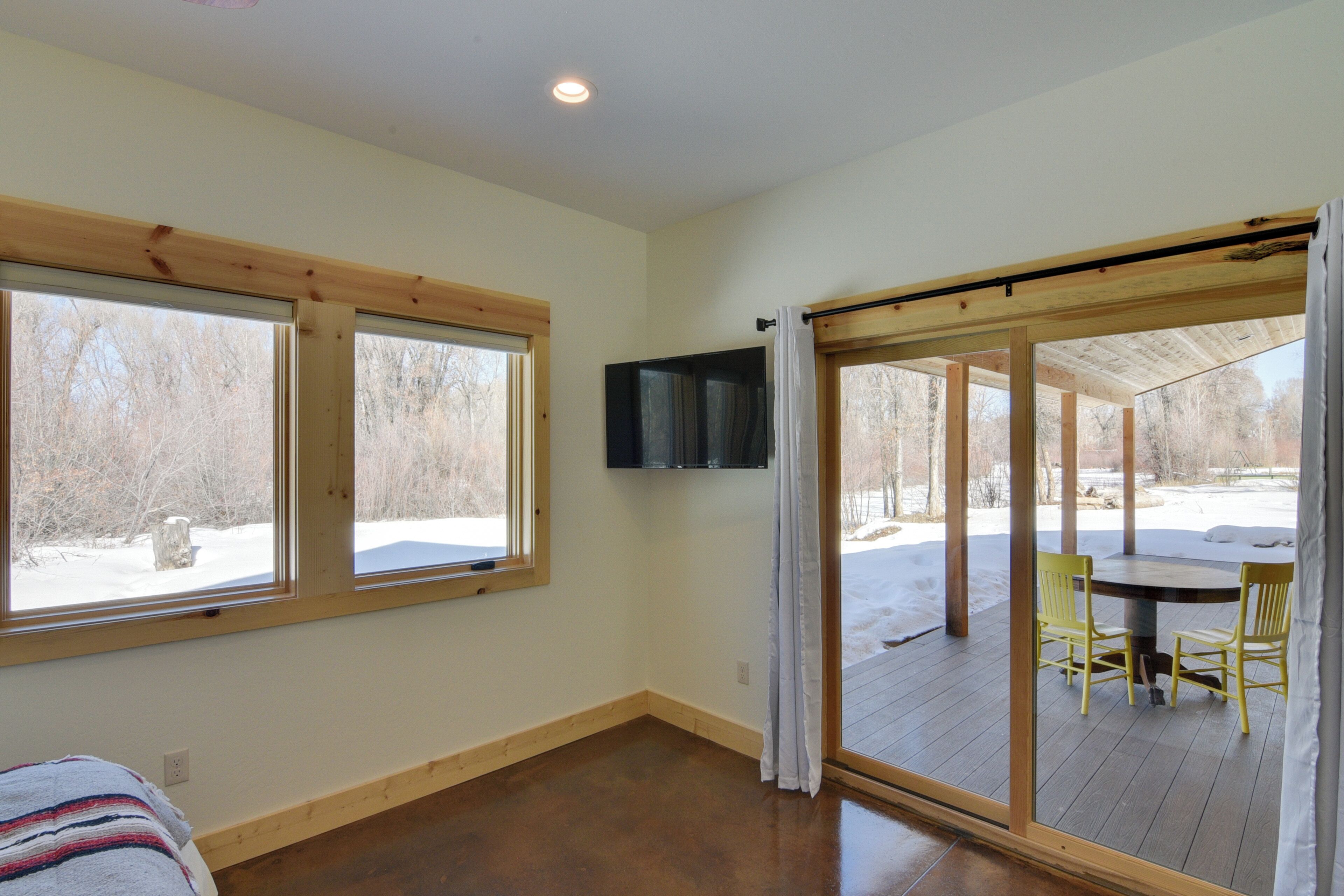 A room with a bed, a TV mounted on the wall, and a sliding glass door leading to an outdoor deck with chairs.