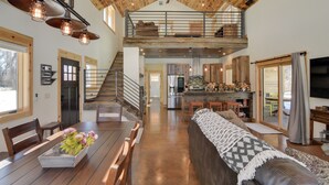 A spacious loft-style living area with a high ceiling, exposed wooden beams, a dining table with chairs, a sofa, and a kitchen area with a large island. - Riverfront Home w/ Bbq: 2 Mi to Downtown Gunnison! (Gunnison)