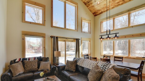 A spacious living room with a large leather sofa, multiple windows, and a dining area. - Riverfront Home w/ Bbq: 2 Mi to Downtown Gunnison! (Gunnison)