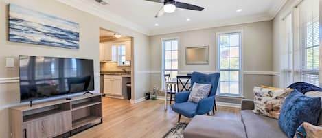 A spacious living room with a flat-screen TV, a ceiling fan, a sofa, and a dining area in the background.