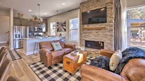 A modern living room with a fireplace, leather furniture, and a kitchen area with stainless steel appliances. - Woodland Park Escape: Licensed, Hot Tub, Mtn Views (Woodland Park)
