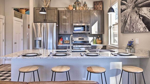 A modern kitchen with granite countertops, stainless steel appliances, and wooden bar stools. - Woodland Park Escape: Licensed, Hot Tub, Mtn Views (Woodland Park)