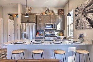 A modern kitchen with granite countertops, stainless steel appliances, and wooden bar stools. - Woodland Park Escape: Licensed, Hot Tub, Mtn Views (Woodland Park)