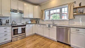 Een moderne keuken met witte kastjes, een roestvrijstalen oven, een vaatwasser en een raam met uitzicht op een woning.