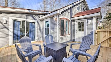 A deck with a table and four Adirondack chairs, surrounded by a house with large windows and a covered patio area.
