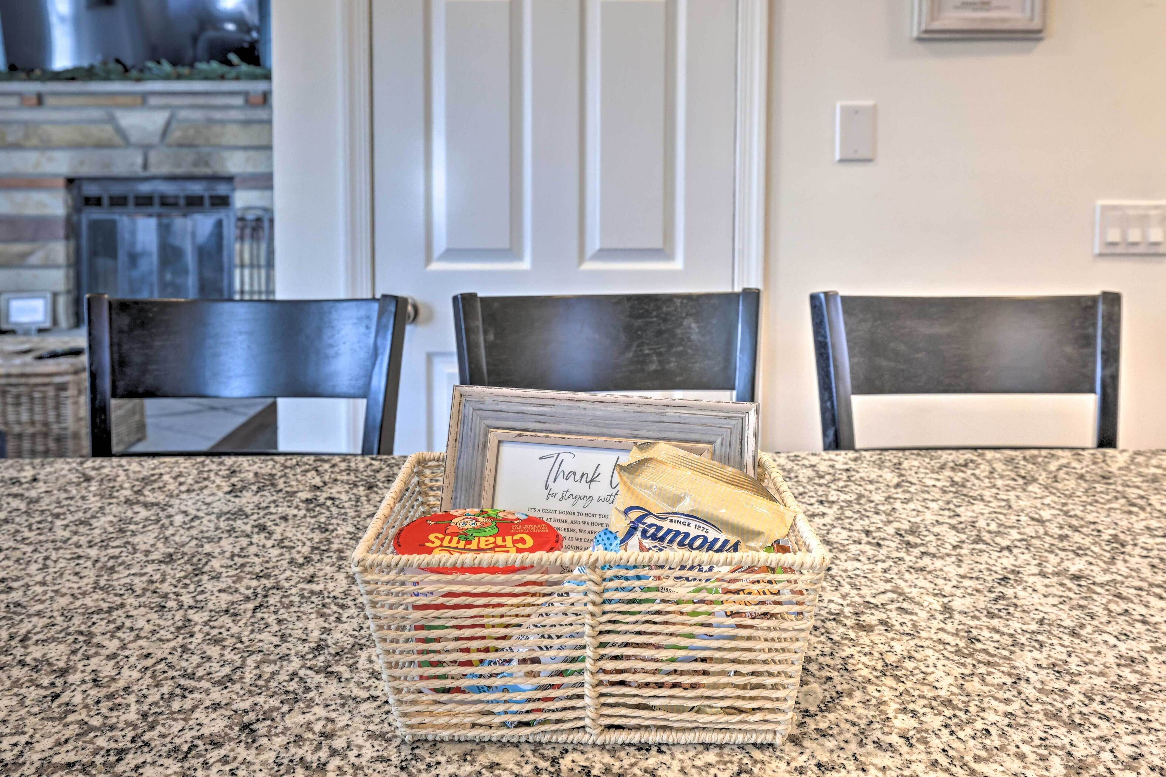 A kitchen with granite countertops, two dark chairs, a wicker basket with food items, and a framed thank you note.