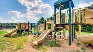 A playground with multiple slides and climbing structures, surrounded by grass and trees. - Bull Shoals Lake Home at Beaver Creek Marina! (Kissee Mills)