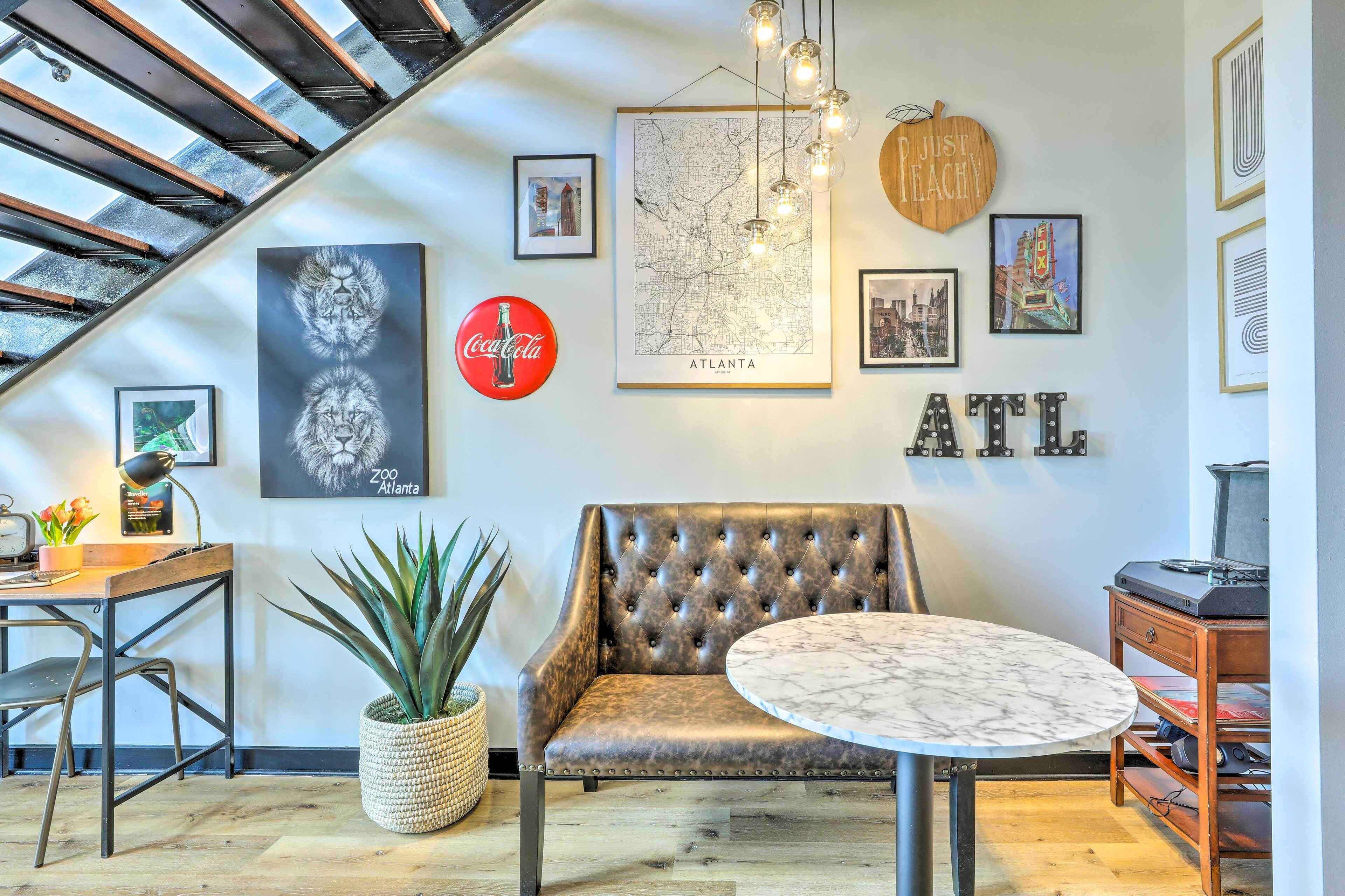 A modern living room with a leather sofa, a round table, a map of Atlanta, and various framed pictures on the wall.