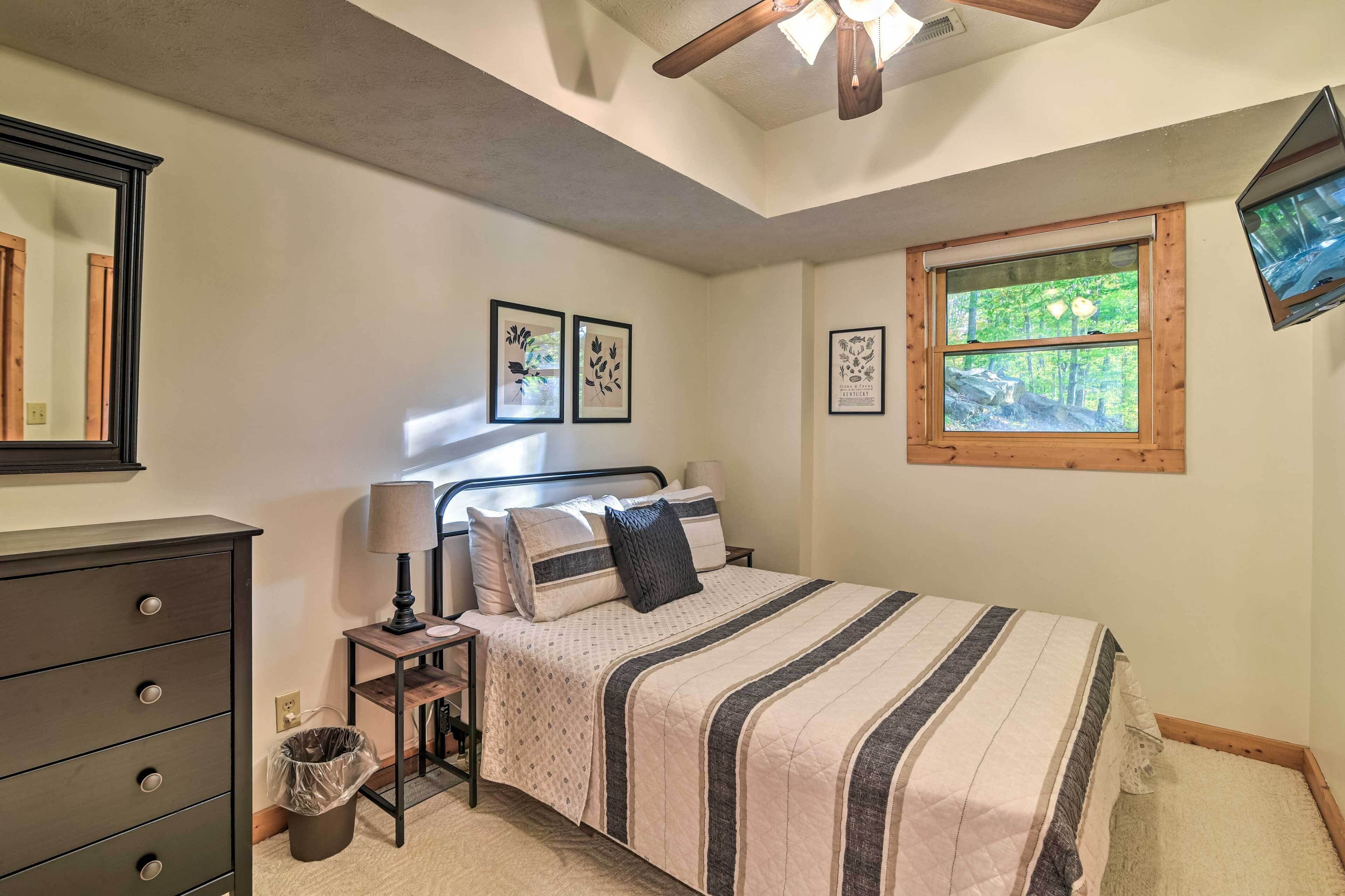 A bedroom with a bed, dresser, lamp, and window with a view of trees.