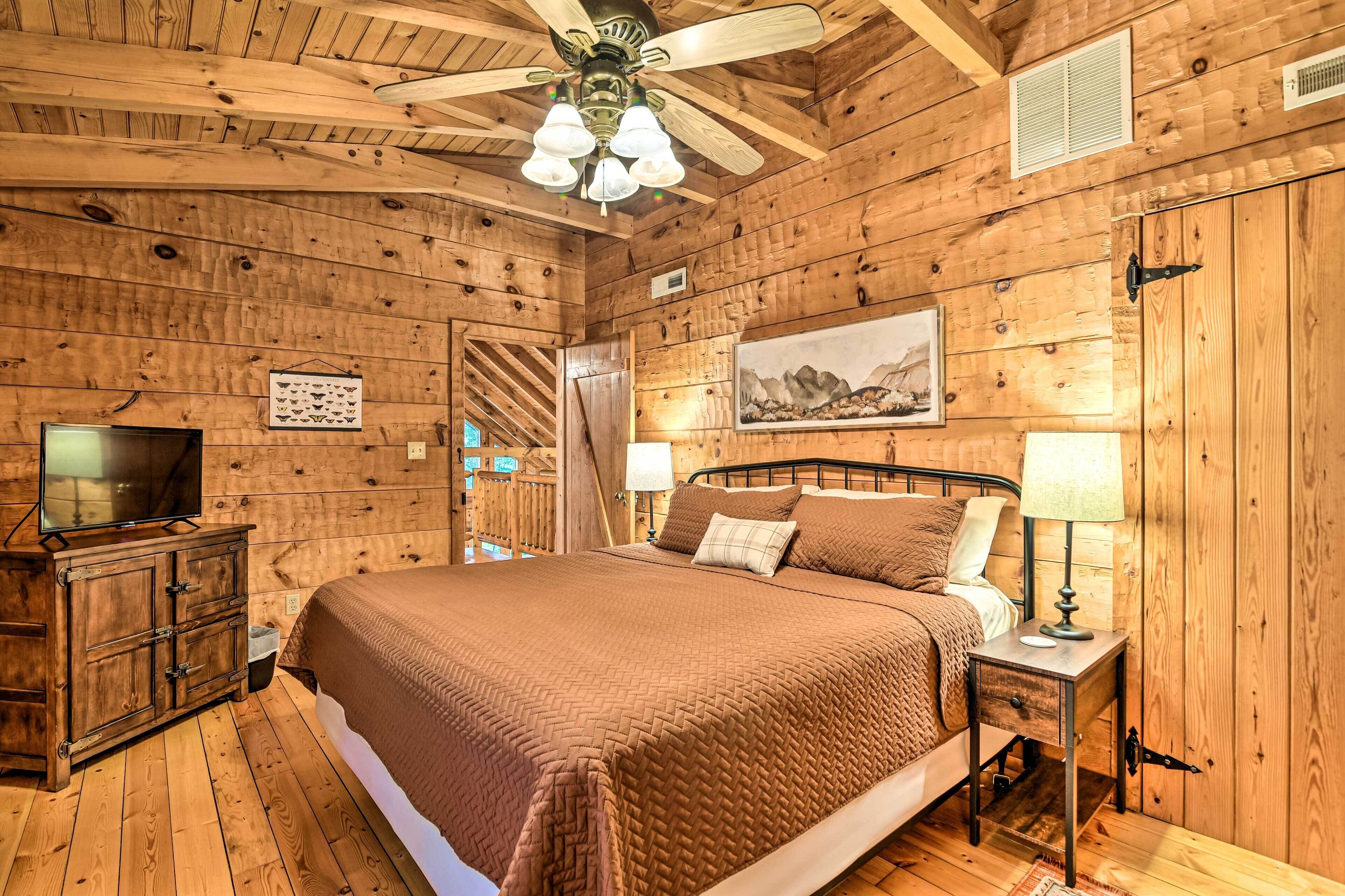 Un dormitorio de cabaña de madera con una cama, mesitas de noche, un televisor y un ventilador de techo.