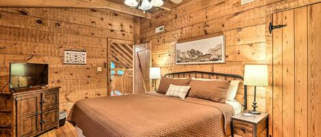 Un dormitorio de cabaña de madera con una cama, mesitas de noche, un televisor y un ventilador de techo.