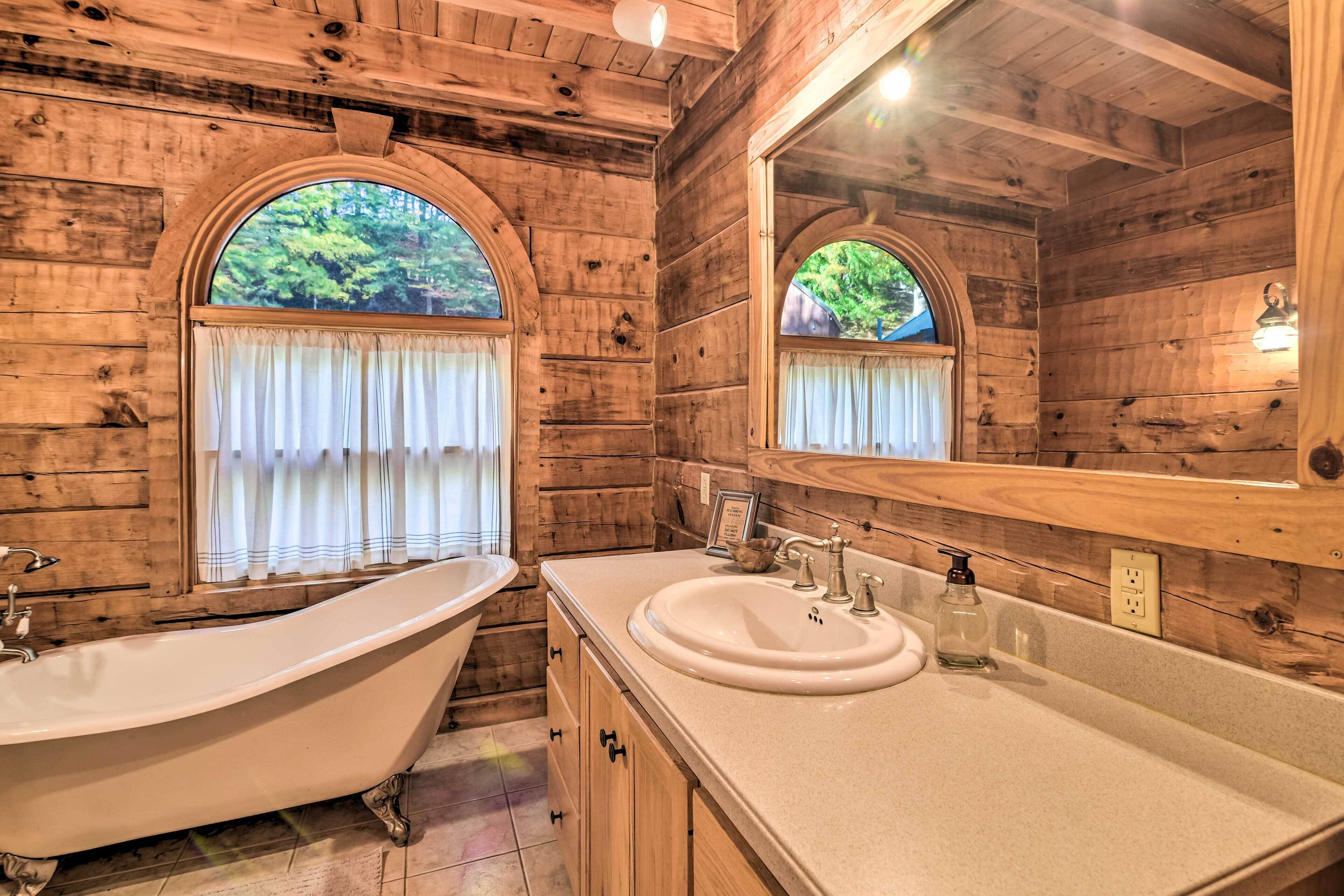 Une salle de bain rustique, avec des murs en bois, comprenant une baignoire sur pieds, un lavabo et un grand miroir.