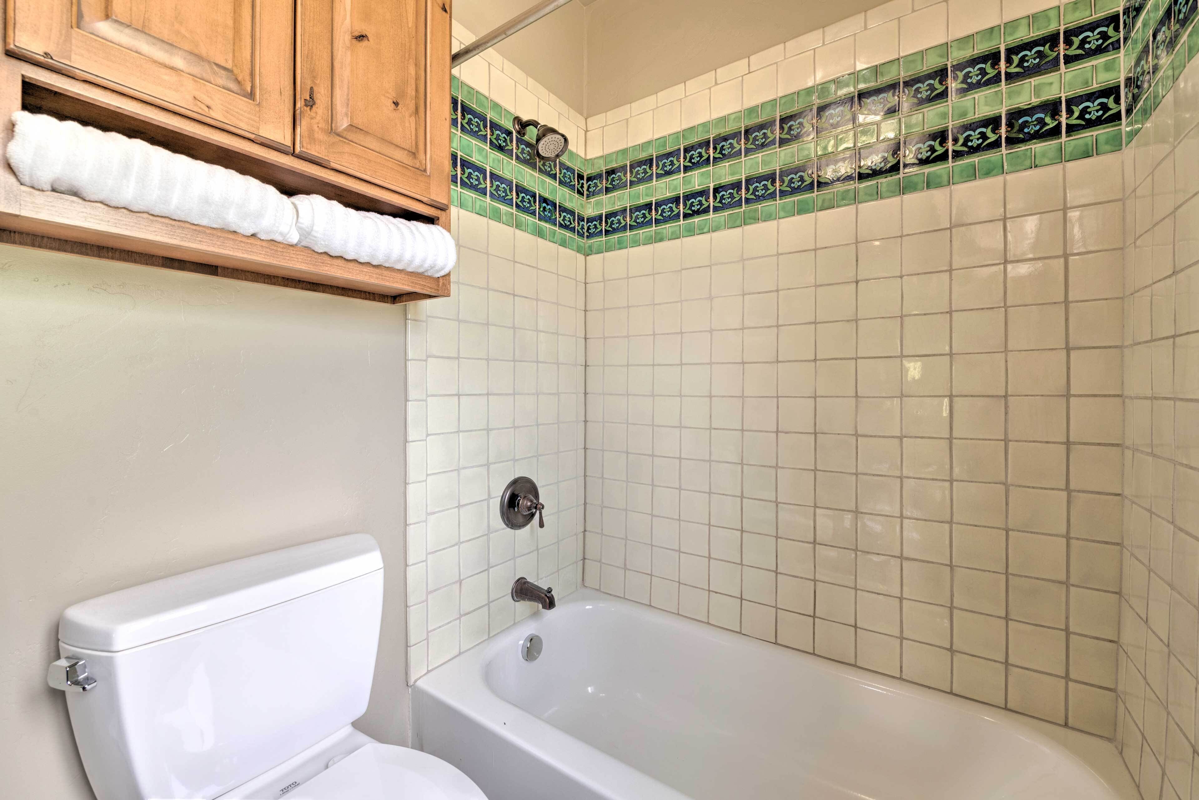 A bathroom with a white bathtub, a toilet, and a shelf with a rolled-up towel.
