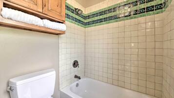 A bathroom with a white bathtub, a toilet, and a shelf with a rolled-up towel.