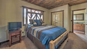 Ein Schlafzimmer mit Holzboden, einem Bett mit blau-brauner Streifenoptik, einem Fernseher auf einem Holzständer und einem Holzschrank.