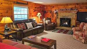 A cozy log cabin-style living room with a fireplace, leather sofas, and a television. - Serene Mountain Retreat on 40 Acres w/ Fire Pit! (Bomont)
