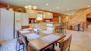 A kitchen with wooden cabinets, a dining table with chairs, a refrigerator, and a staircase leading to an upper level. - Serene Mountain Retreat on 40 Acres w/ Fire Pit! (Bomont)