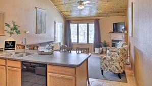 A kitchen with a dishwasher, a dining area with a table and chairs, a sofa, and a television in the living room. - Riverfront Crivitz Condo w/ Fireplace & Views (Crivitz)