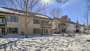 A residential building with multiple balconies, a covered patio, and a snow-covered yard. - Riverfront Crivitz Condo w/ Fireplace & Views (Crivitz)