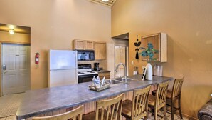 A kitchen with a central island, wooden chairs, a refrigerator, a microwave, and a sink. - Riverfront Crivitz Condo w/ Fireplace & Views (Crivitz)