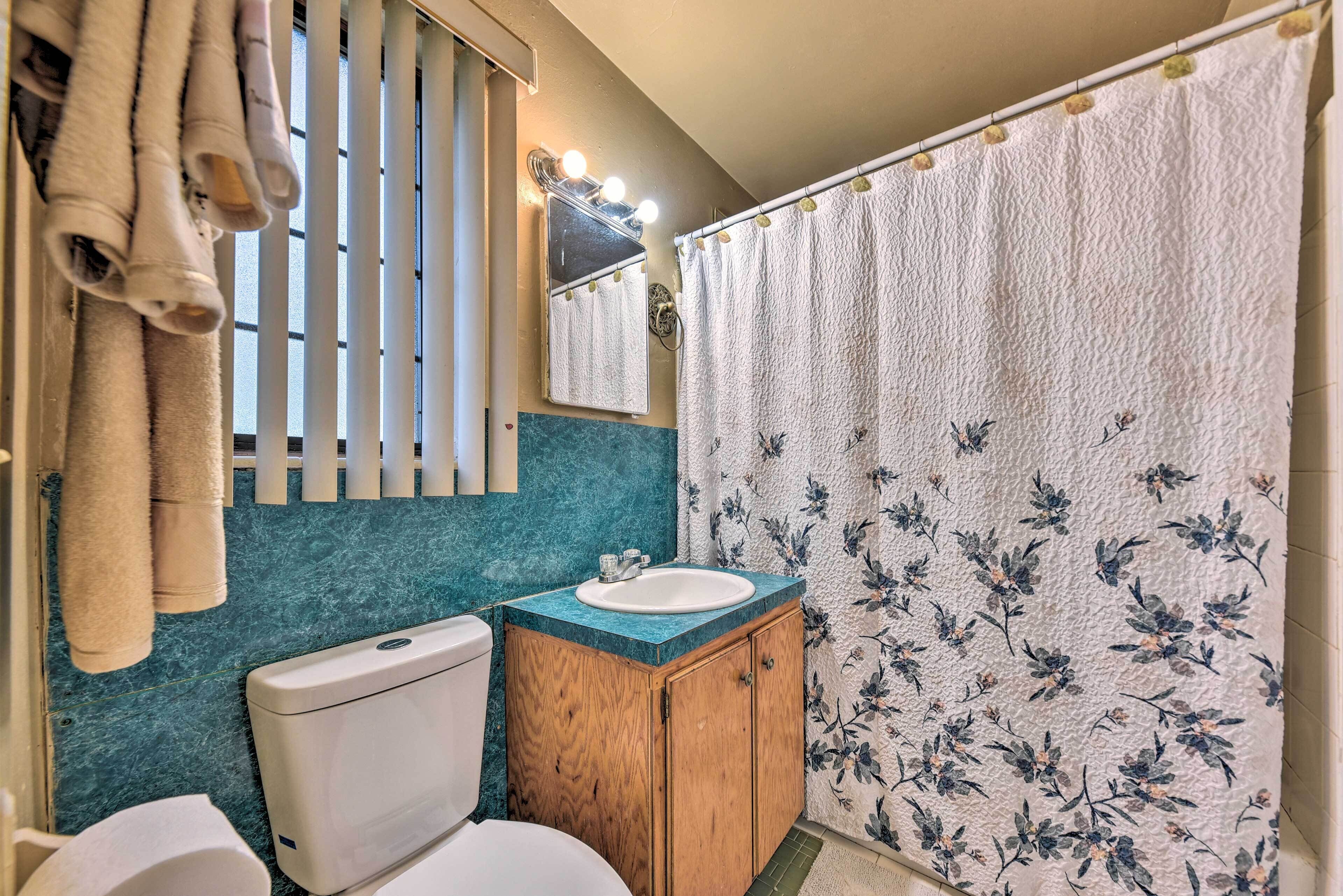 A bathroom with a toilet, a sink, a wooden cabinet, and a shower curtain with a floral pattern.