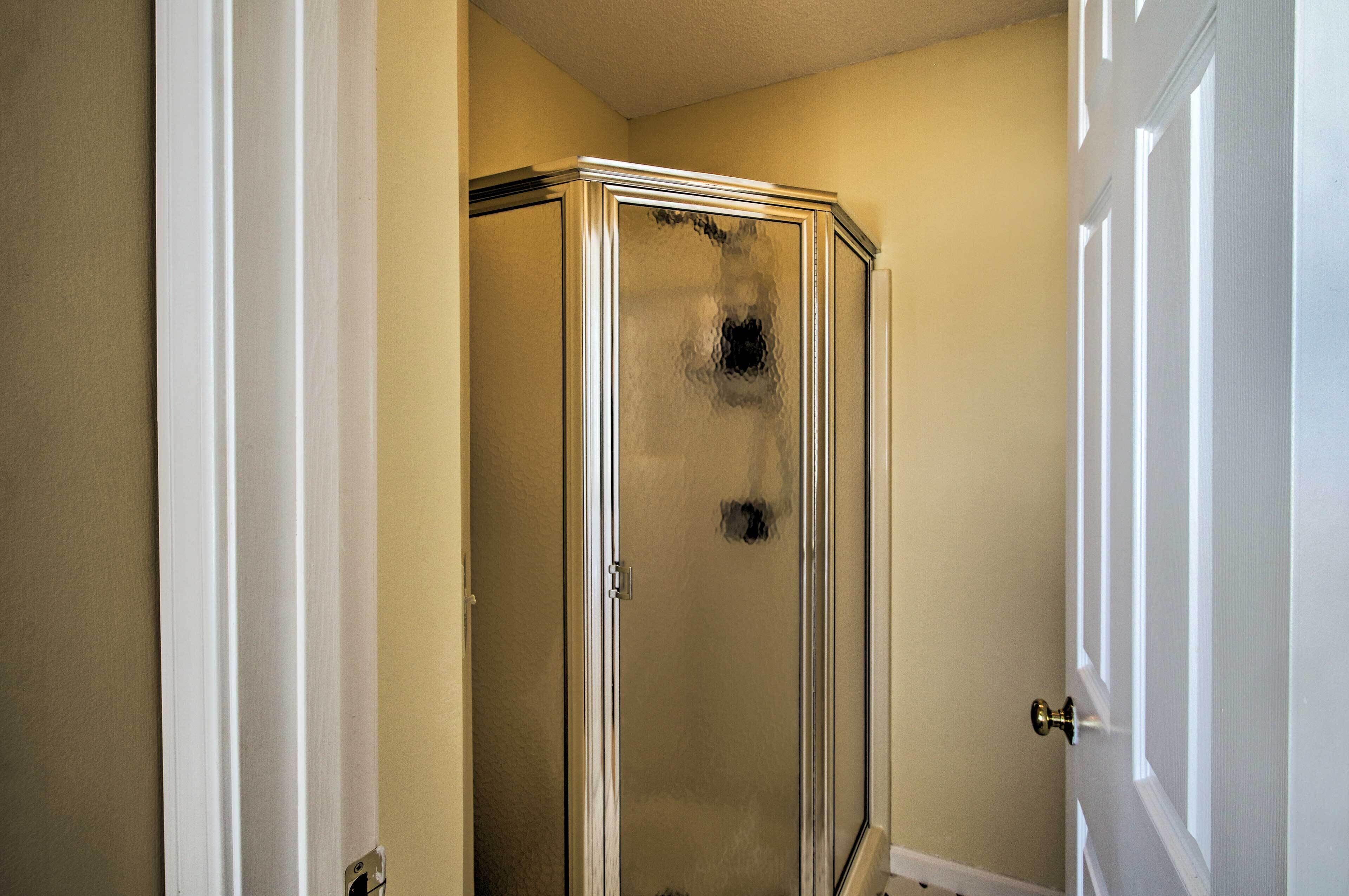 A bathroom with a glass shower enclosure, a white door, and beige walls.