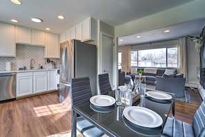 A modern kitchen with white cabinets, a large refrigerator, and a dining area with a glass table set for four.