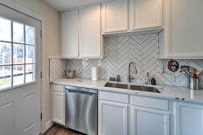 A kitchen with white cabinets, a herringbone tile backsplash, a stainless steel dishwasher, and a sink with a faucet.