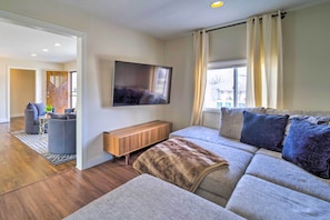 A modern living room with a large sofa, a wooden bench, and a flat-screen TV mounted on the wall.
