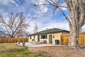 Ein eingeschossiges Haus mit überdachter Terrasse, Holzzaun und einem großen Baum im Garten.