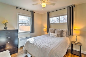 A bedroom with a bed, two bedside lamps, a dresser, a window with curtains, and a ceiling fan.