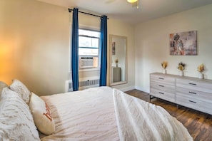 Ein Schlafzimmer mit einem Bett, einem Schminktisch, einem Fenster mit Vorhängen, einer Heizung und einem Bild an der Wand.