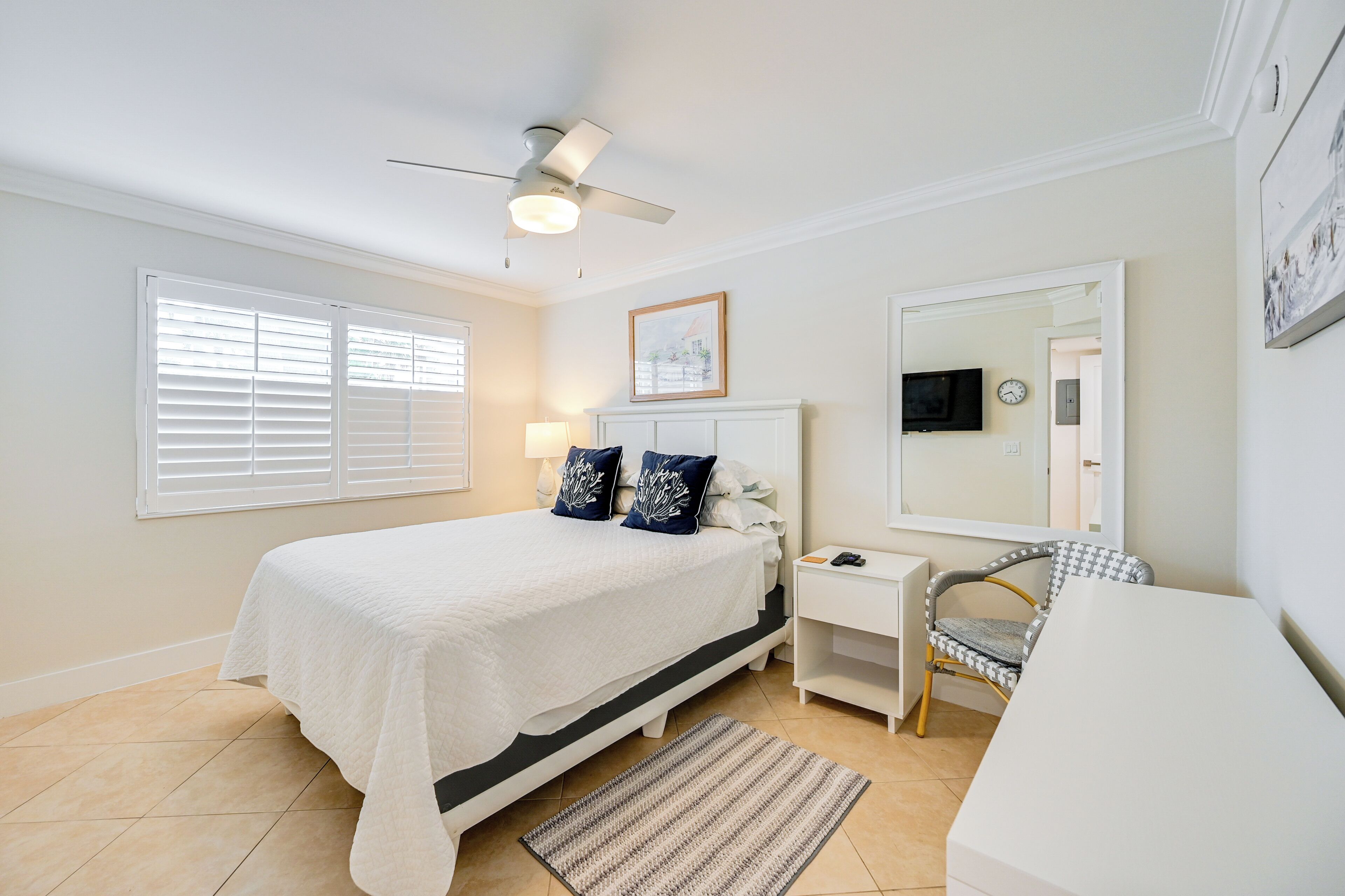 A bedroom with a bed, bedside table, chair, and a ceiling fan.