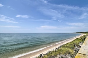 Une plage avec une promenade en béton longeant le rivage, un ciel dégagé et une eau calme.