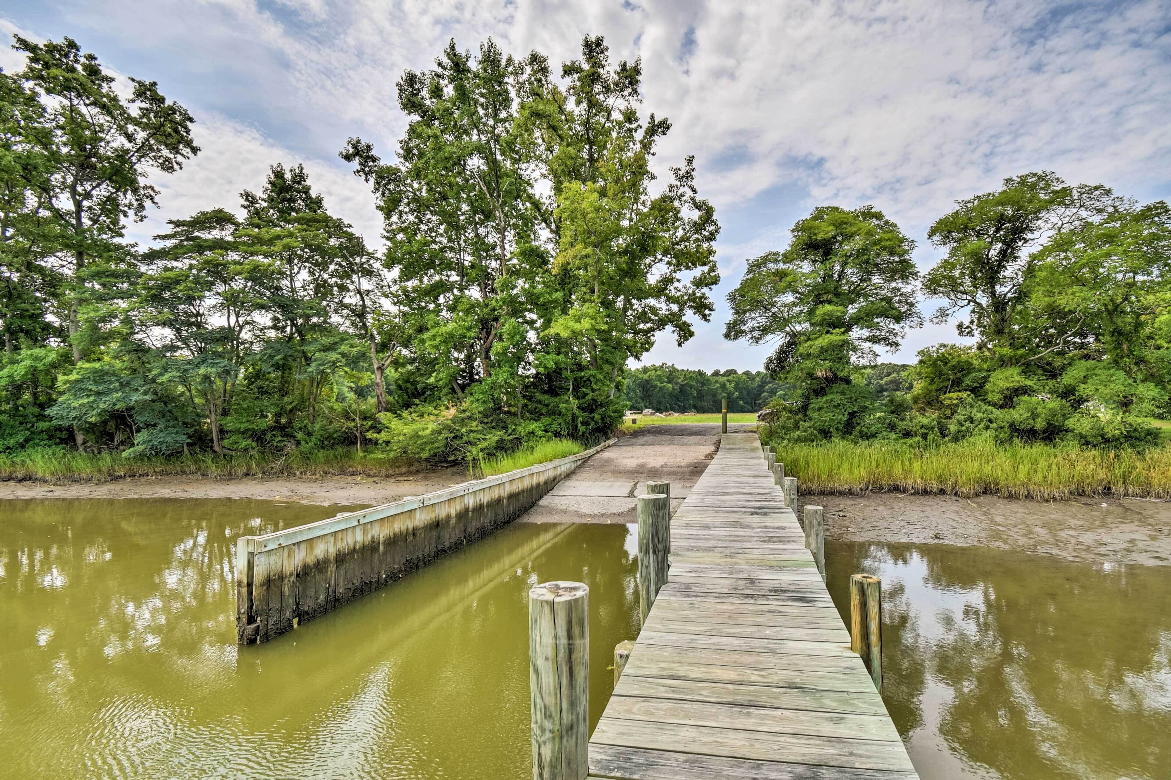 A wooden boardwalk over a calm water body, surrounded by dense greenery and trees.